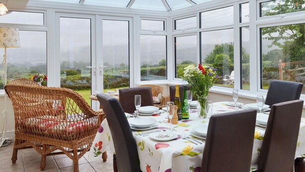 A conservatory with a table set for dining, wicker chairs, and a view of the garden. - 3 bedroom accommodation in Llangenny, near Crickhowell (Llangenny, near Crickhowell)