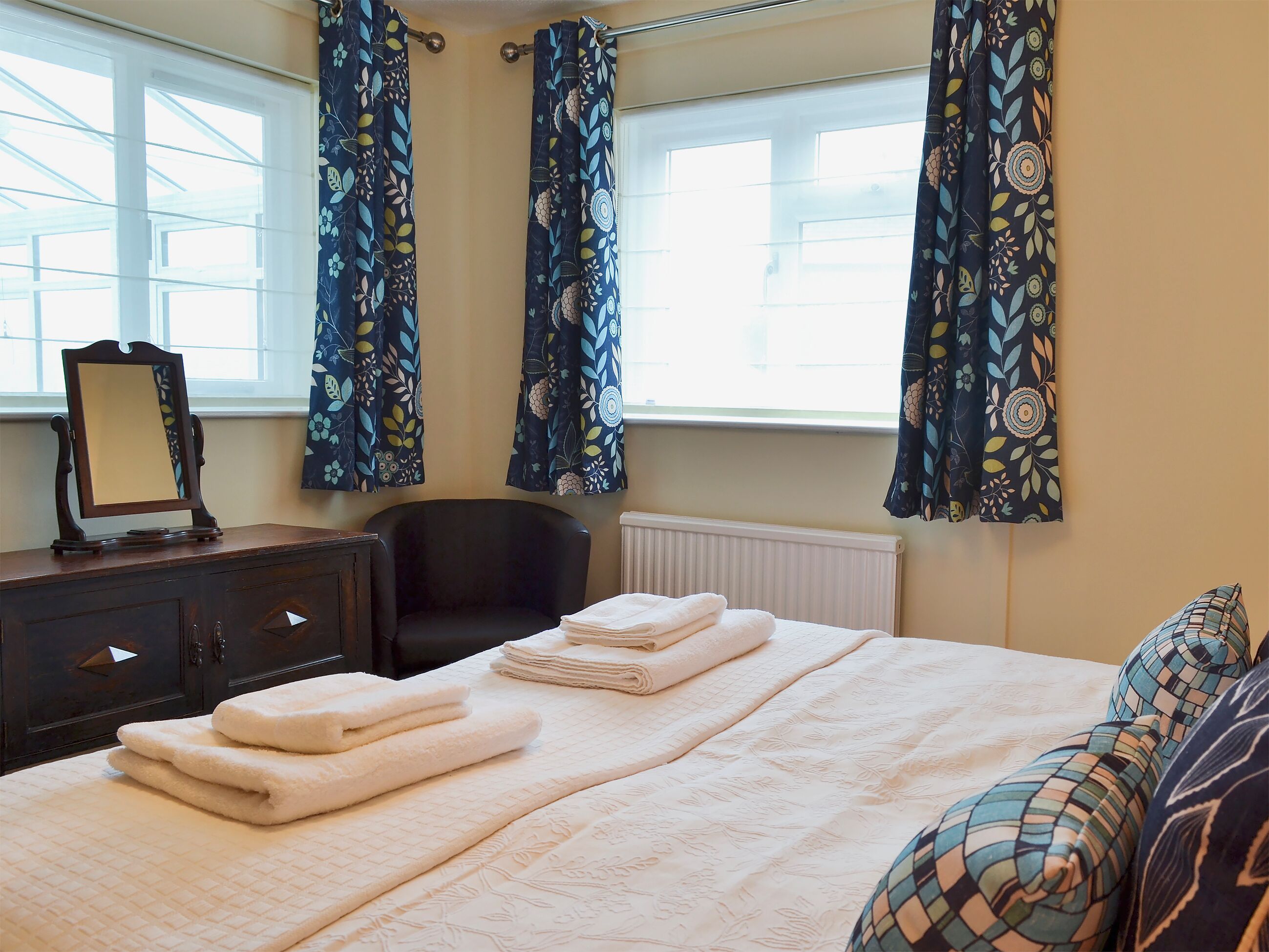 Une chambre à coucher avec un lit, une chaise, une commode et une fenêtre avec des rideaux.