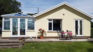 A single-story house with a conservatory, a patio with a table and chairs, and a small garden area. - 3 bedroom accommodation in Llangenny, near Crickhowell (Llangenny, near Crickhowell)