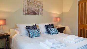 A neatly made bed with white linens and two patterned pillows, flanked by bedside tables with lamps, in a room with a large painting on the wall.