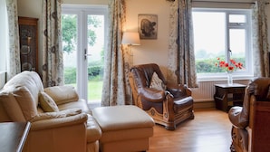 A living room with a leather armchair, a sofa, and a wooden coffee table. There is a window with curtains, a lamp, and a vase with flowers. - 3 bedroom accommodation in Llangenny, near Crickhowell (Llangenny, near Crickhowell)