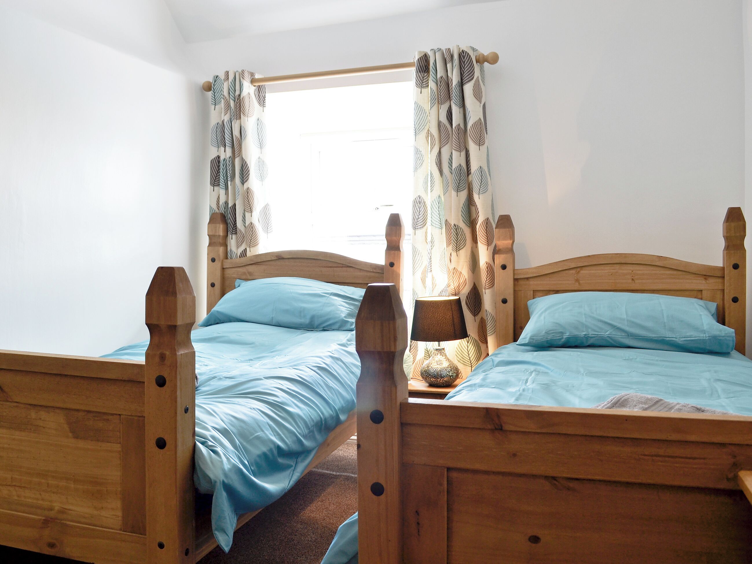 A room with two wooden beds, each with a headboard and footboard, and a window with leaf-patterned curtains.