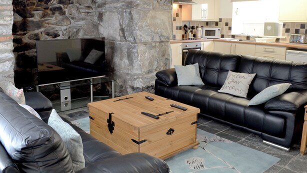 Ein gemütlicher Wohnbereich mit Steinwand, einem schwarzen Ledersofa, einem Holztisch und einem Fernseher.