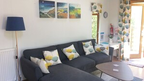 A living room with a sofa set, a coffee table, a lamp, and three paintings on the wall. - 1 bedroom accommodation in Instow, near Barnstaple (Instow, near Barnstaple)