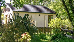 A house with a sloped roof, surrounded by lush greenery and a wooden fence. - 1 bedroom accommodation in Instow, near Barnstaple (Instow, near Barnstaple)