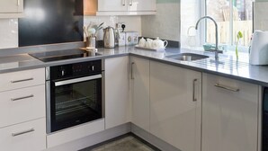 A modern kitchen with white cabinets, stainless steel appliances, and a window providing a view of the outside. - 2 bedroom accommodation in Belford, near Alnwick (Belford, near Alnwick)