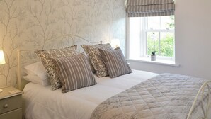 A neatly made bed with a quilted cover, a bedside table with a lamp, and a window with a view of greenery. - 2 bedroom accommodation in Belford, near Alnwick (Belford, near Alnwick)