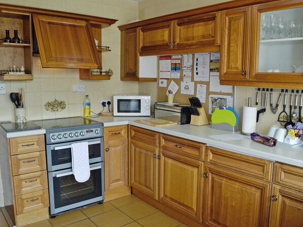 A kitchen with wooden cabinets, a stove, microwave, and various kitchen utensils.
