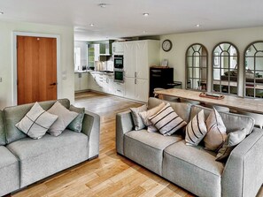 A modern living room with two grey sofas, wooden flooring, a kitchen in the background, and a dining area with a wooden table. - 5 bedroom accommodation in Cirencester (Cirencester)