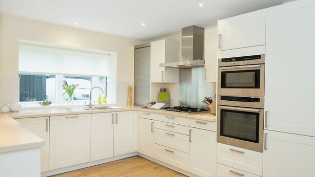 Una cocina moderna con gabinetes blancos, campana de acero inoxidable, dos hornos y un ventanal con vistas.