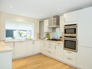 A modern kitchen with white cabinets, a stainless steel range hood, double ovens, and a window with a view. - 5 bedroom accommodation in Cirencester (Cirencester)