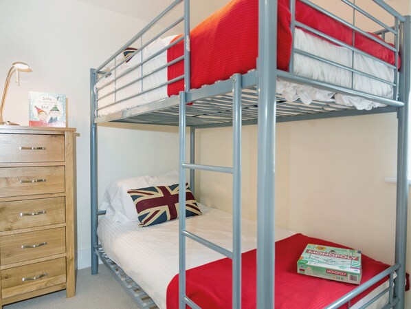 A bunk bed with a red blanket, a wooden dresser with drawers, and a Monopoly board game.