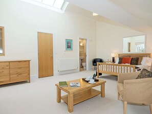 A spacious living room with a wooden coffee table, a sofa, a chair, and a large mirror. - 5 bedroom accommodation in Cirencester (Cirencester)