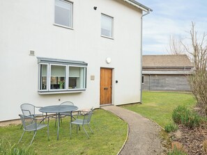 A white house with a wooden door, a window with a view, and a patio with metal chairs and a table. - 5 bedroom accommodation in Cirencester (Cirencester)