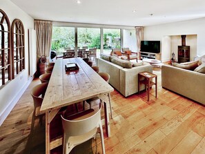 A spacious living room with a wooden dining table, a sofa, and a TV. - 5 bedroom accommodation in Cirencester (Cirencester)