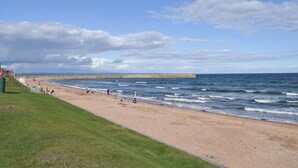 A beach with a grassy area, a sandy shore, and a stone sea wall. - 4 bedroom accommodation in Balmullo, near St Andrews (Balmullo, near St Andrews)