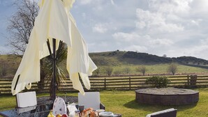 An outdoor dining area with a table set for breakfast, a wicker chair, and a white umbrella providing shade. - 4 bedroom accommodation in Balmullo, near St Andrews (Balmullo, near St Andrews)