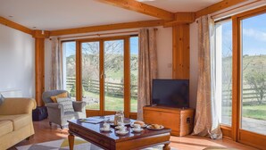 A spacious living room with a wooden ceiling, large windows, a television, and a coffee table with cups and saucers. - 4 bedroom accommodation in Balmullo, near St Andrews (Balmullo, near St Andrews)