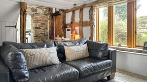 Un sofá de cuero negro con cojines a rayas en una habitación rústica con paredes de piedra, vigas de madera y vistas amplias a través de grandes ventanales.