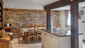 Uma cozinha com parede de tijolos, cadeiras de madeira, bancada de mármore e chão revestido de azulejos.