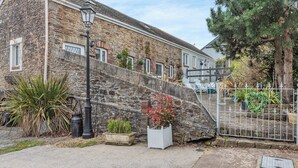 A stone building with a staircase leading to a gated area, surrounded by potted plants and a metal fence. - 0 bedroom accommodation in Gowerton, Gower (Gowerton, Gower)