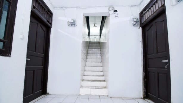 Un passadís amb sòl de rajoles blanques, una escala i dues portes fosques.