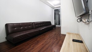 Una habitació amb un sofà de pell marró, una taula de fusta i una televisió penjada a la paret.