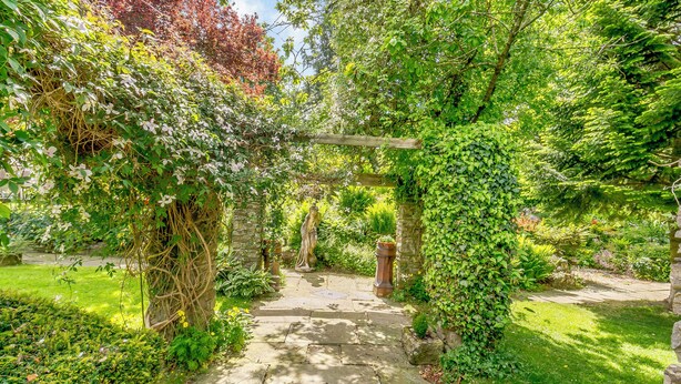 A stone pathway leading through a lush garden with a wooden archway and a statue. - 2 bedroom accommodation in West Burton, near Leyburn (West Burton, near Leyburn)