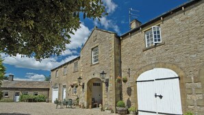 A stone building with a gravel driveway, a white door, and hanging flower baskets. - 2 bedroom accommodation in West Burton, near Leyburn (West Burton, near Leyburn)