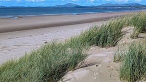 Een strand met duinen en een helder uitzicht op de oceaan en verre bergen.
