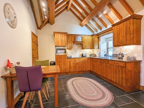 A kitchen with wooden cabinets, a built-in oven, a dining table with chairs, and a rug on the floor.