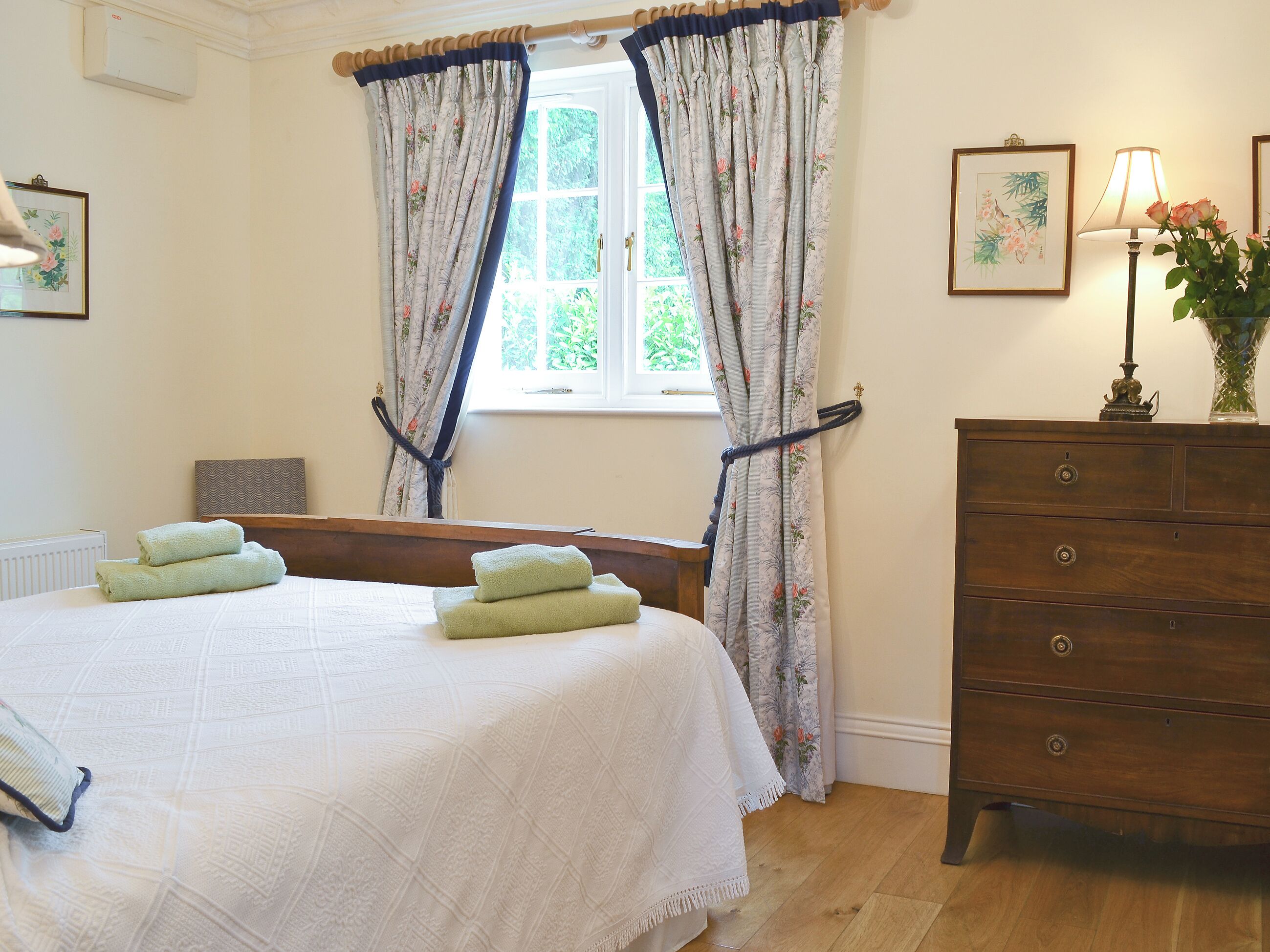 A bedroom with a bed, a dresser, a window with curtains, and a lamp.