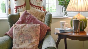 Une pièce chaleureuse avec un fauteuil vert, une lampe, une cafetière et un vase rempli de fleurs.