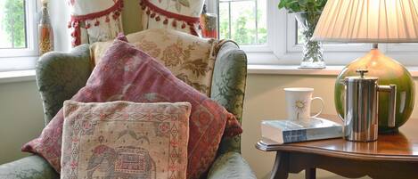 A cozy room with a green armchair, a lamp, a coffee pot, and a vase with flowers.