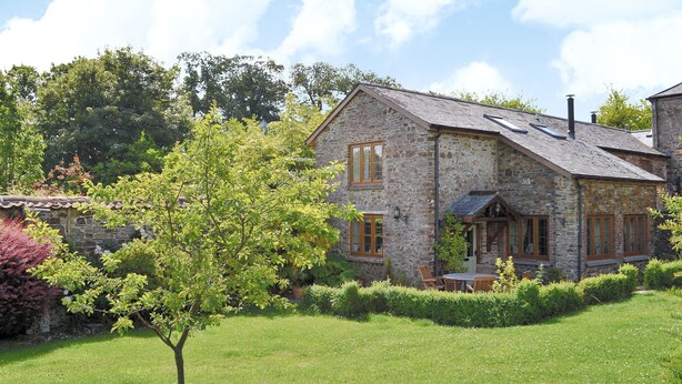 Une maison en pierre avec un toit à deux versants, un petit porche et une pelouse bien entretenue.