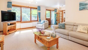 A living room with a TV, sofa, coffee table, and a view of the outdoors. - Glen View of Enrick House (Balnain near Drumnadrochit)