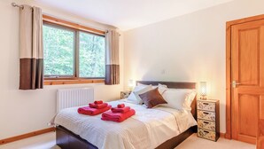 A neatly made bed with red towels, a bedside lamp, and a view of greenery through a window. - Glen View of Enrick House (Balnain near Drumnadrochit)