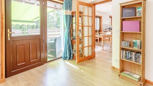 A spacious room with a wooden door, a sliding glass door leading to a balcony, and a bookshelf filled with books. - Glen View of Enrick House (Balnain near Drumnadrochit)