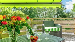 A covered outdoor seating area with wicker furniture, a table with a glass vase of flowers, and a bottle of water. - Glen View of Enrick House (Balnain near Drumnadrochit)