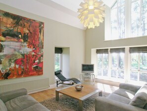 A modern living room with a large abstract painting, a black lounge chair, a coffee table with a bowl, and a television.