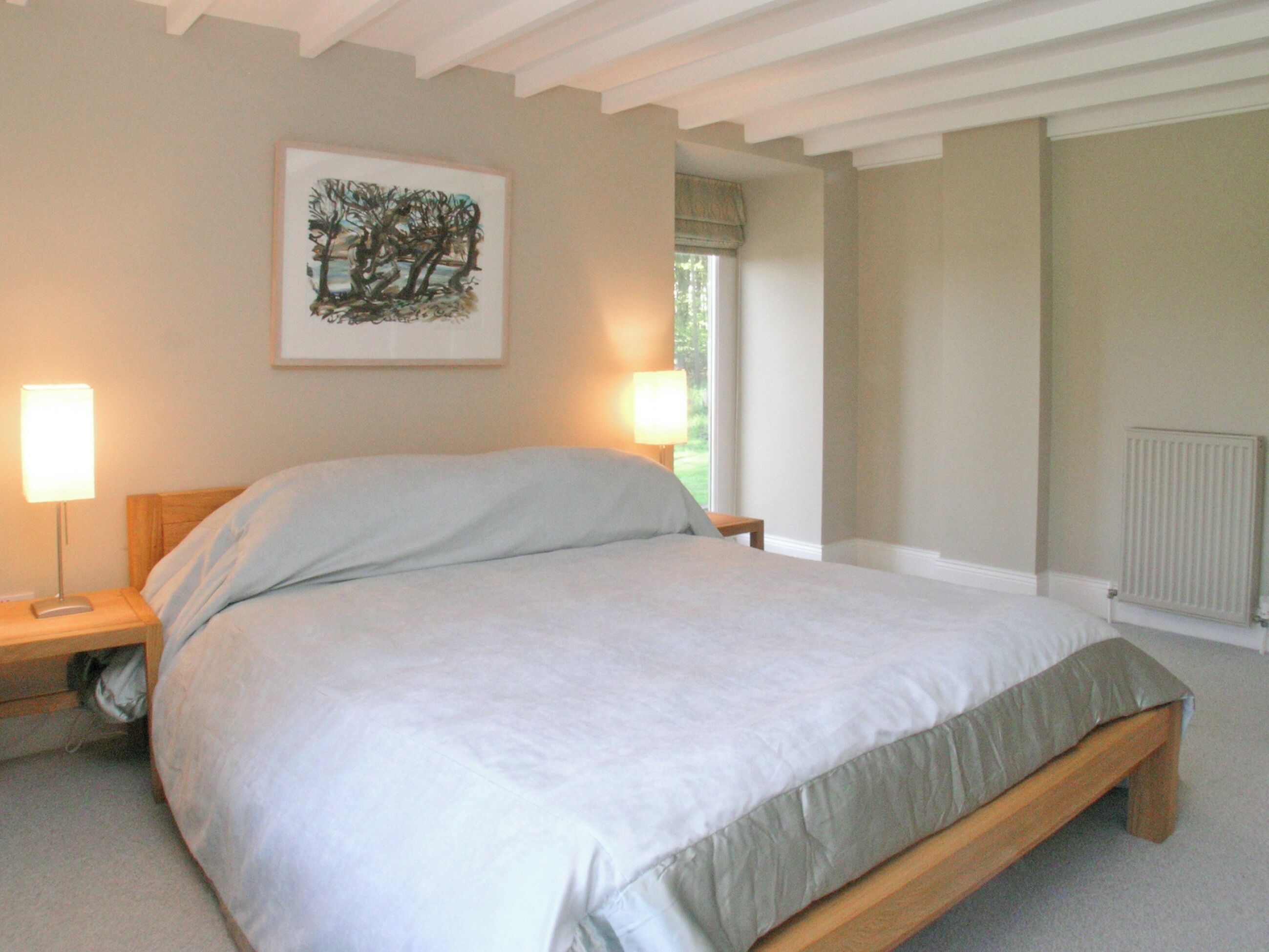 A bedroom with a bed, bedside lamps, a window with a view, and a radiator.