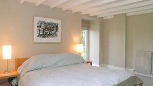 Quarto com cama, luminárias de cabeceira, janela com vista e radiador.