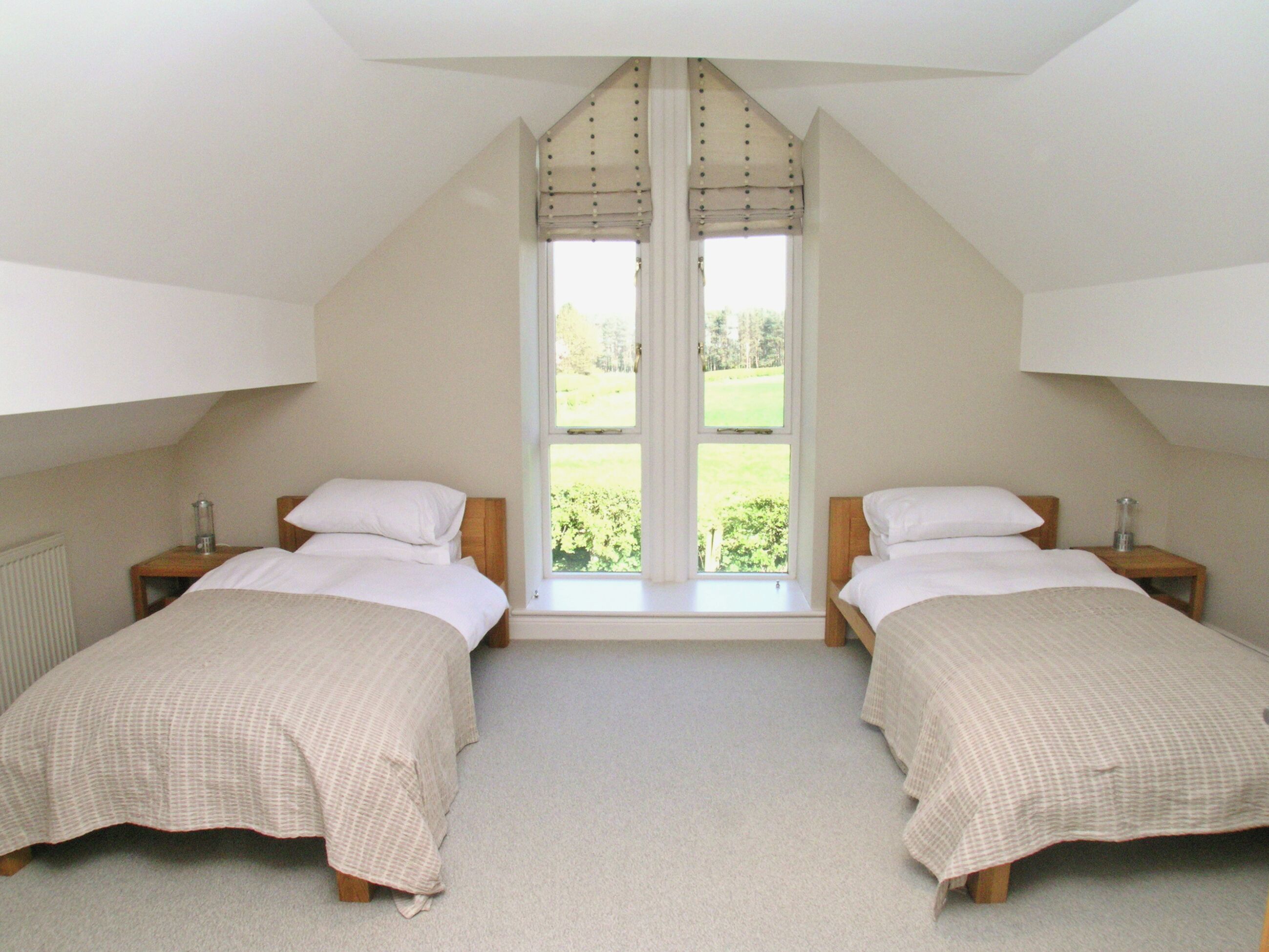 A bedroom with two beds, a large window, and a sloped ceiling.