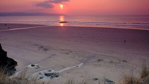 Ein Strand bei Sonnenuntergang mit klarem Himmel, ruhiger See und fernen Bergen.