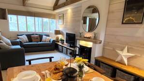 Ein gemütliches Wohnzimmer mit einer Couch, einem Fernseher, einem Kamin und einem Essbereich mit einem für das Frühstück gedeckten Tisch.