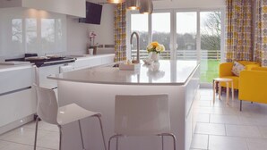 A modern kitchen with a central island, white chairs, a yellow sofa, and large windows offering a view of the outdoors. - 3 bedroom accommodation in New Moat, near Narberth (New Moat, near Narberth)