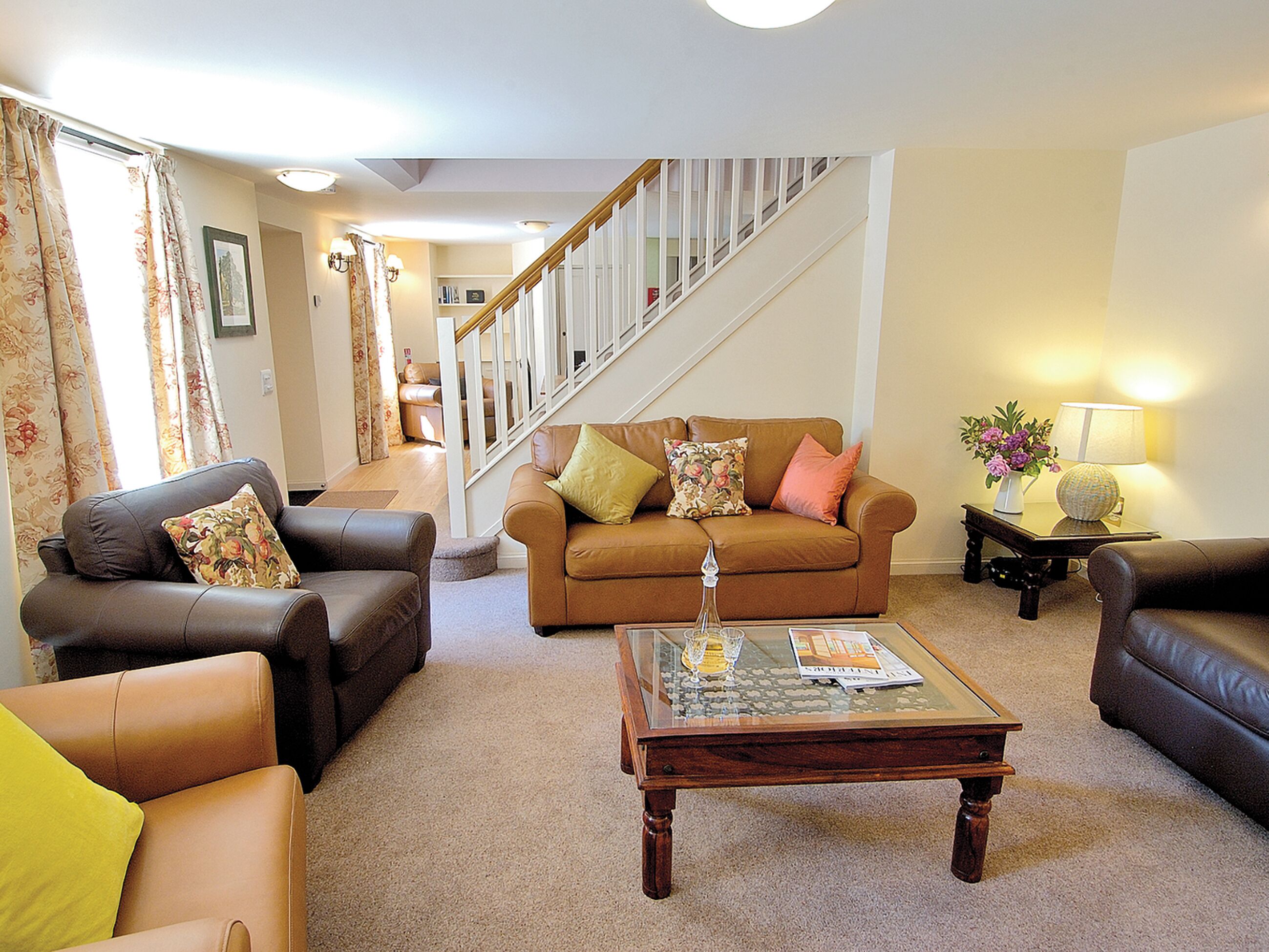 A living room with a brown sofa, two armchairs, a coffee table, and a staircase.