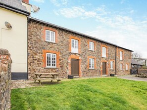 A stone building with multiple windows and doors, a picnic table, and a grassy area in front. - Granary Cottage - E5634 (Chittlehampton, near Umberleigh)
