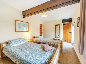 A room with two beds, a wooden ceiling beam, a painting, a mirror, and a door. - Granary Cottage - E5634 (Chittlehampton, near Umberleigh)