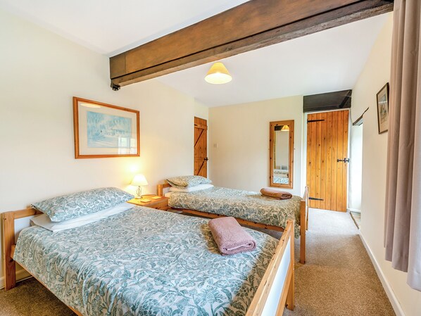 A room with two beds, a wooden ceiling beam, a painting, a mirror, and a door. - Granary Cottage - E5634 (Chittlehampton, near Umberleigh)